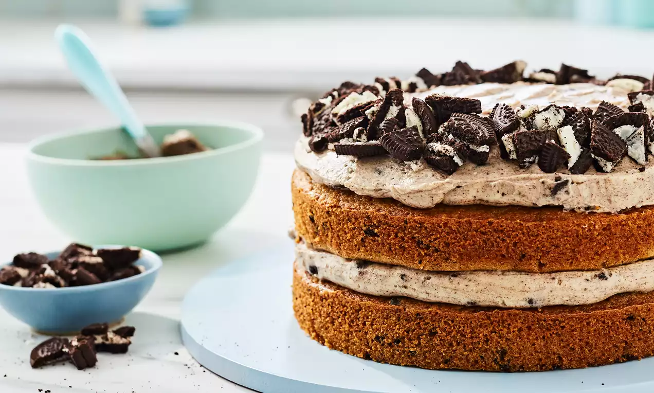 Cookies and Cream cake with two golden sponge layers, speckled light cream filling and topping, crowned with crushed dark cookies